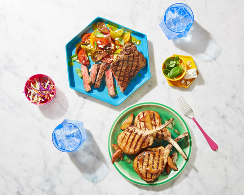 Photo aérienne de côtelettes de porc grillées sur une assiette verte et de longe de porc grillée sur une assiette bleue assise sur une table en marbre blanc