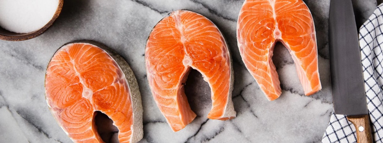 3 pavés de saumon sur une planche à découper en marbre