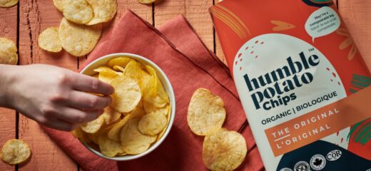 Bowl of Humble Potato chips on wood table top beside a bag of original Humble potato chips